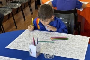 Estudante da rede municipal de ensino da Castro usa lápis de cor para pintar mapa sobre uma mesa azul