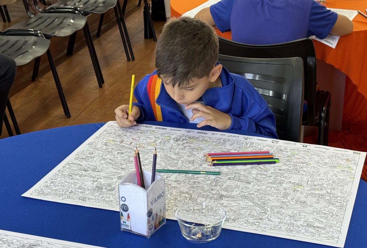 Estudante da rede municipal de ensino da Castro usa lápis de cor para pintar mapa sobre uma mesa azul