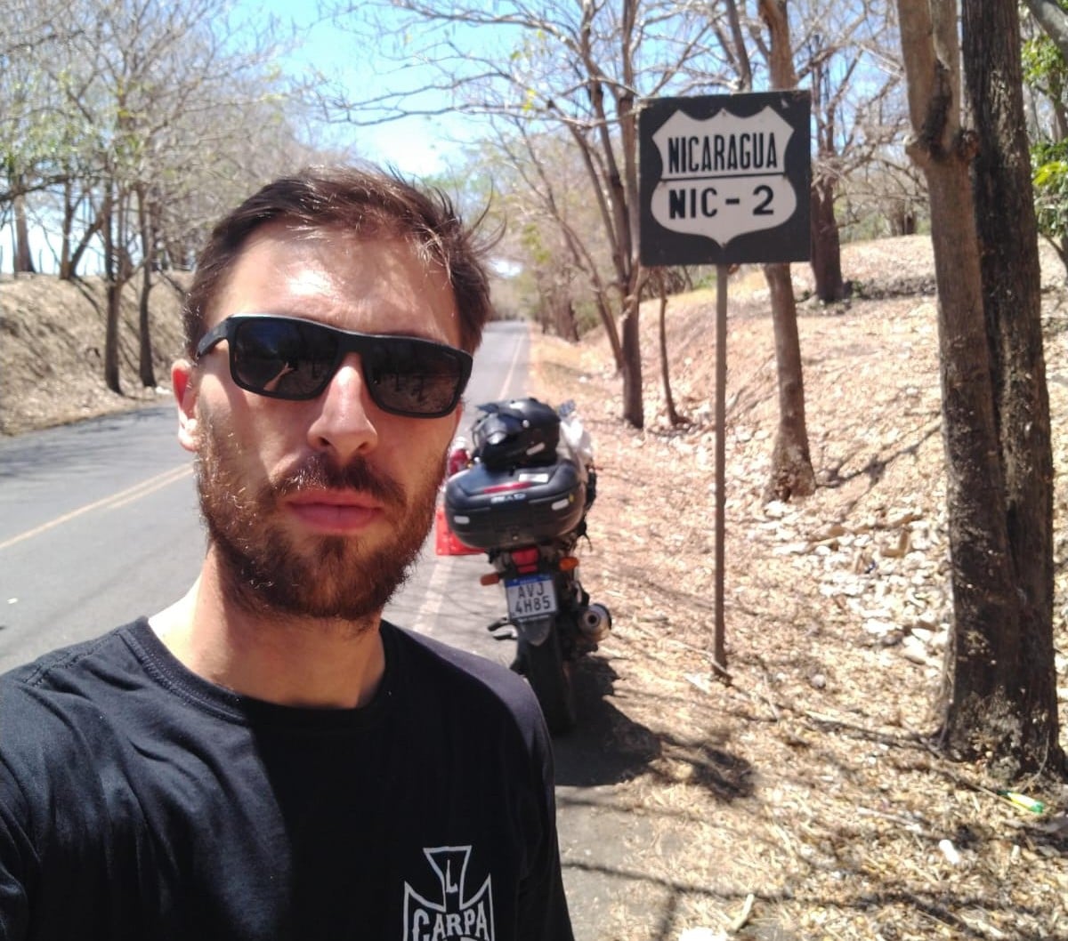 Professor Fred Petla em selfie com uma placa de Nicarágua, ao lado de sua moto