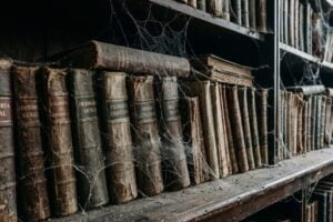 Livros antigos, cobertos por poeira e teias de aranha, em uma estante antiga