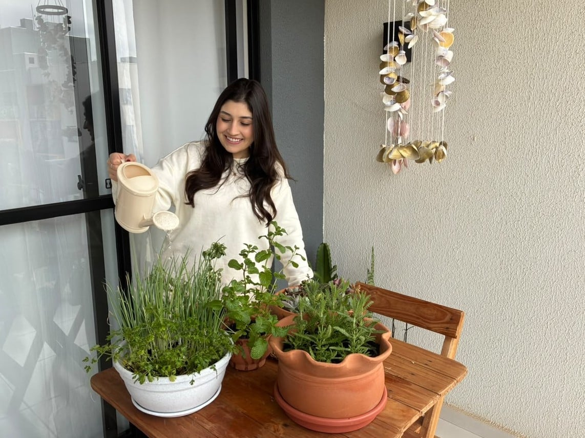 Mulher regando plantas em uma pequena horta em apartamento
