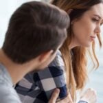 Foto ilustrativa de um casal triste, em que o homem está voltado à mulher, sentados com expressão triste em um fundo acinzentado