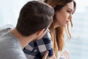 Foto ilustrativa de um casal triste, em que o homem está voltado à mulher, sentados com expressão triste em um fundo acinzentado