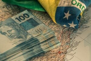 Nortas de cem em cima de uma mapa mundi e a bandeira do Brasil ao lado