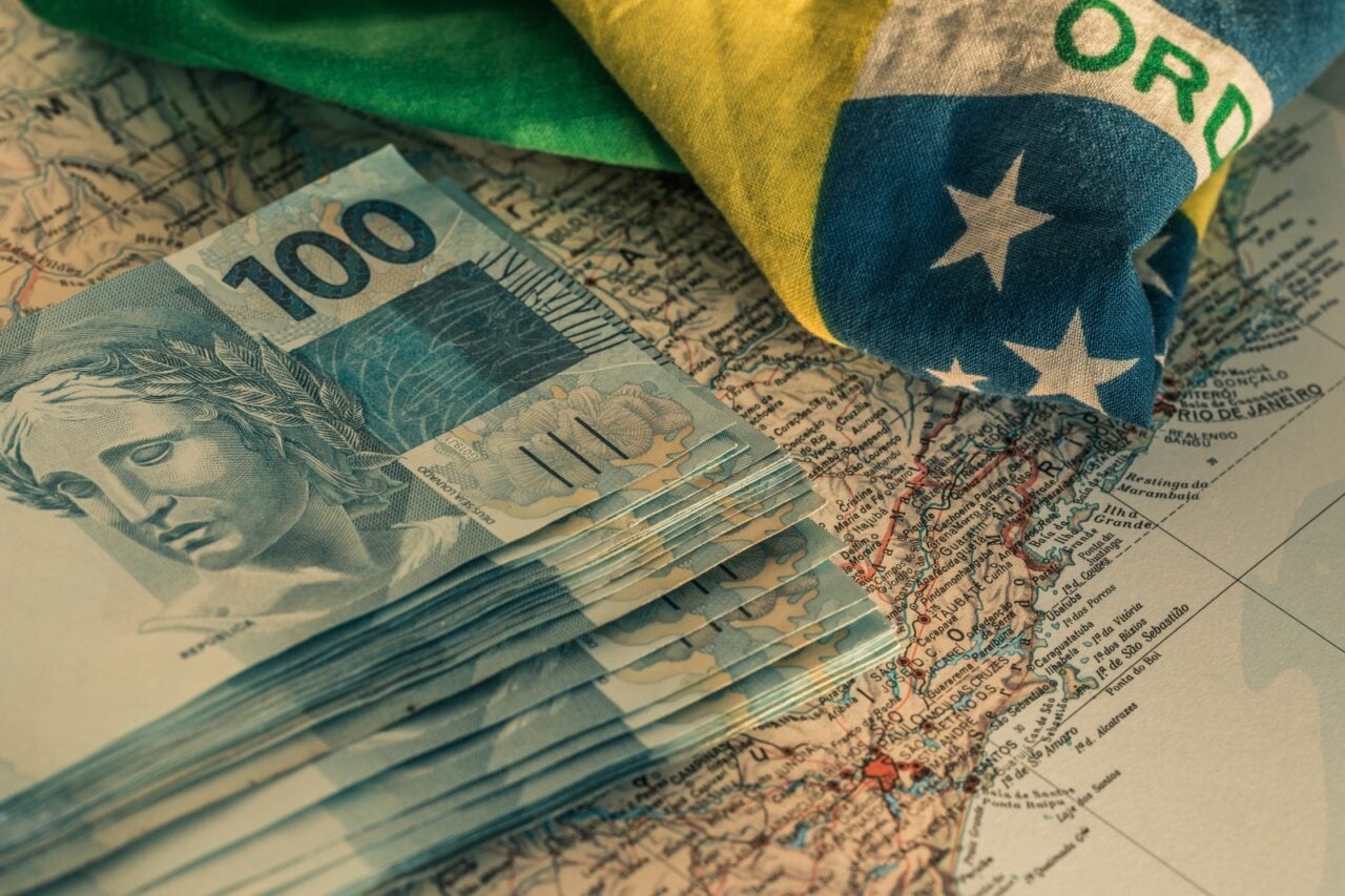 Nortas de cem em cima de uma mapa mundi e a bandeira do Brasil ao lado